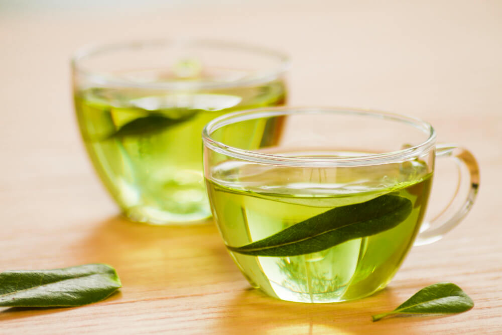 Clear cups of green tea with fresh leaves, packed with antioxidants that detoxify, brighten skin, and enhance natural radiance.