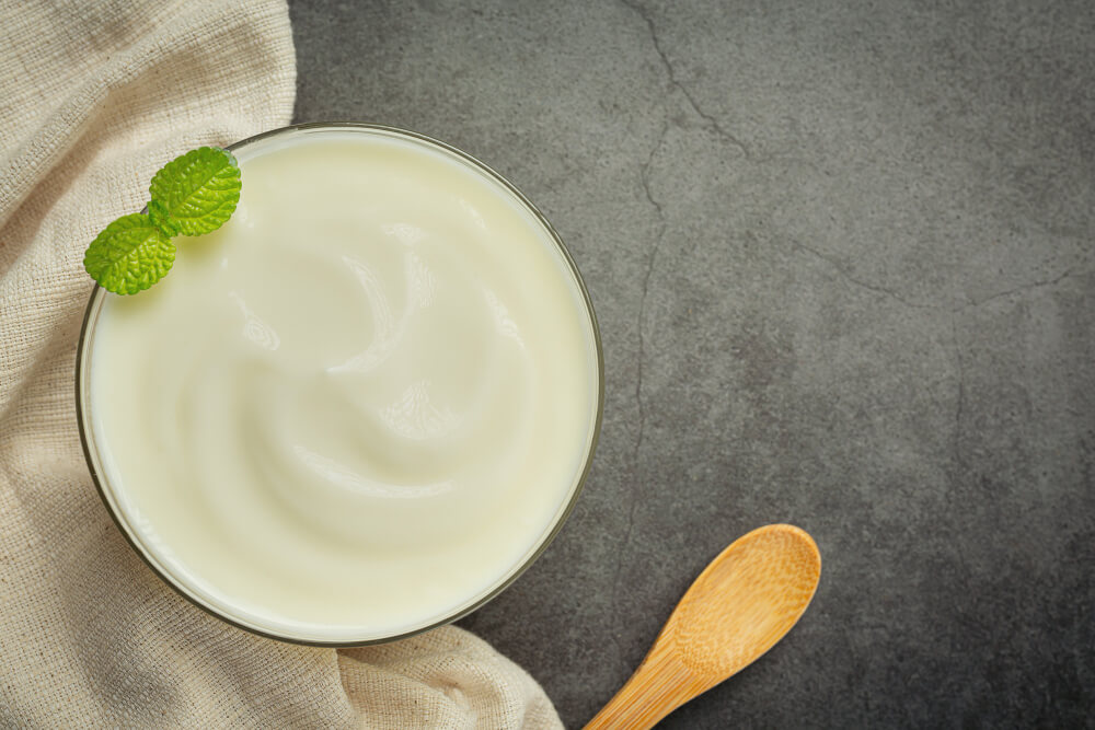 Bowl of plain yogurt with mint garnish, rich in lactic acid that helps lighten skin and improve texture naturally. 